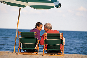 Mature couple smiling at each other sitting on chairs at beach